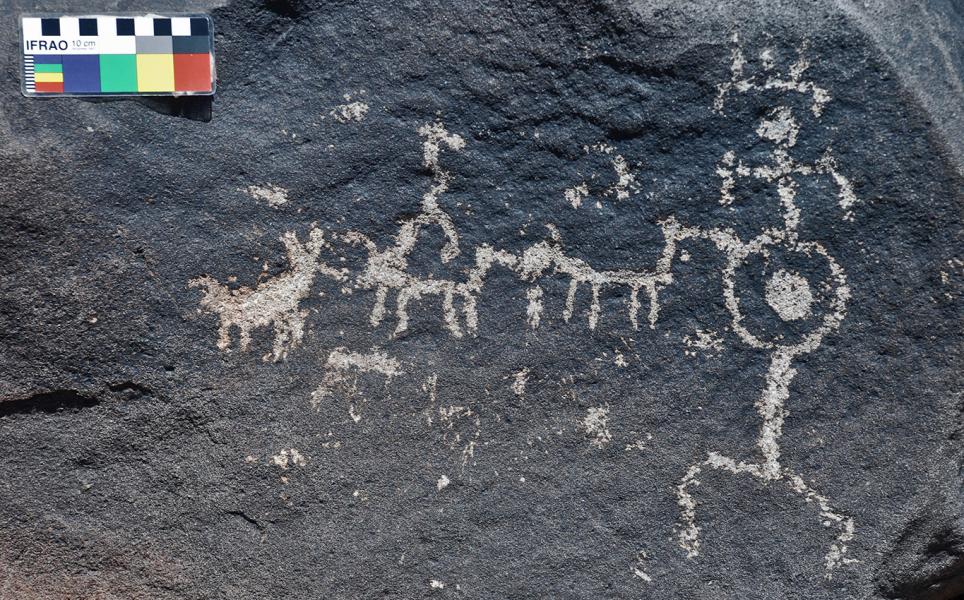 Petroglifo de figura antropomorfa con tocado junto a camélidos